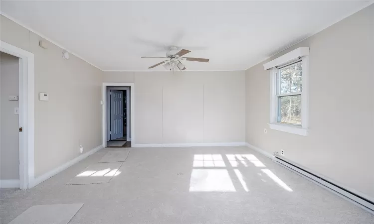 Spare room featuring light carpet, crown molding, ceiling fan, and a baseboard heating unit