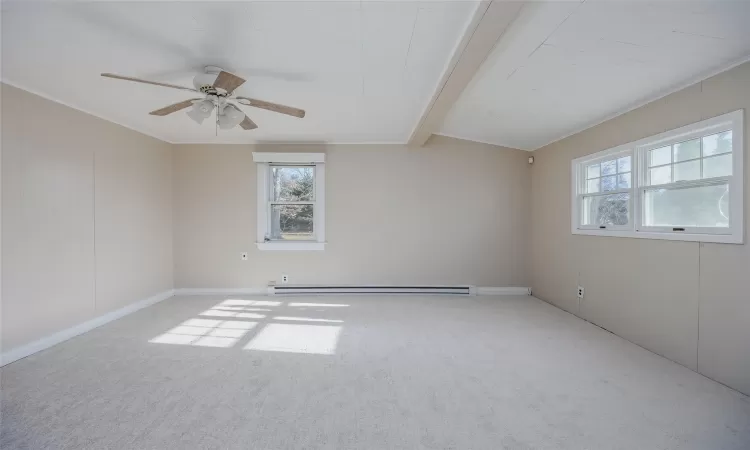 Carpeted empty room featuring ceiling fan, lofted ceiling with beams, crown molding, and a baseboard radiator