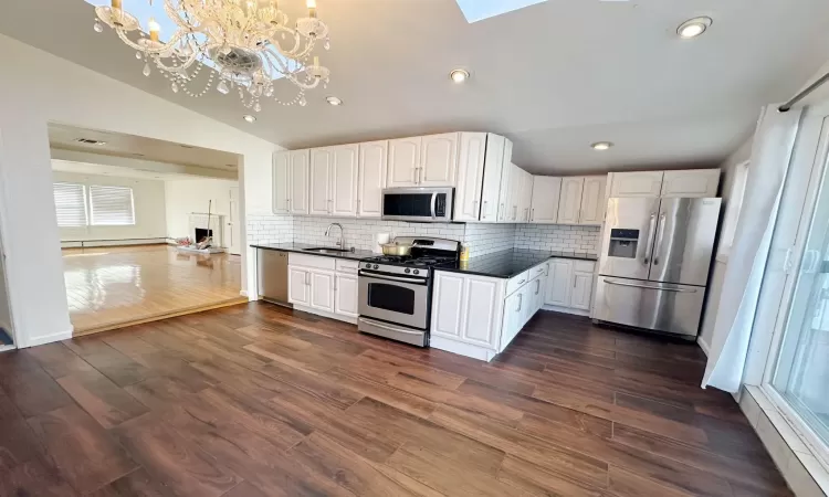 Kitchen with dark wood-type flooring, stainless steel appliances, vaulted ceiling, decorative light fixtures, and white cabinets