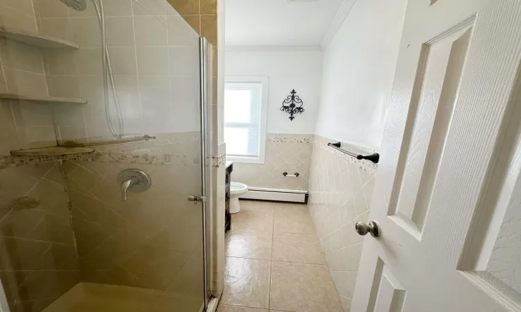 Bathroom featuring a baseboard radiator, tile patterned floors, crown molding, a shower with door, and tile walls