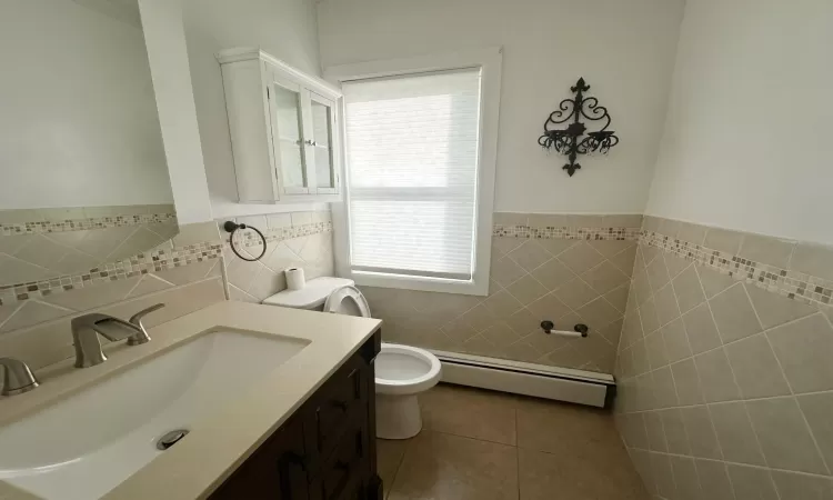 Bathroom featuring vanity, a baseboard radiator, tile walls, tile patterned flooring, and toilet