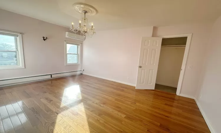 Empty room with plenty of natural light, a wall mounted air conditioner, hardwood / wood-style floors, and a baseboard radiator