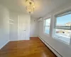 Empty room featuring a wall mounted air conditioner, wood-type flooring, baseboard heating, and a notable chandelier