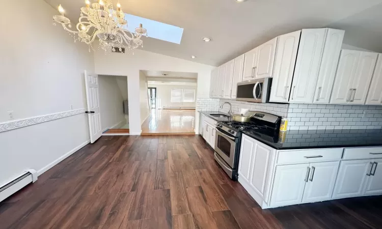 Kitchen featuring appliances with stainless steel finishes, dark hardwood / wood-style flooring, lofted ceiling with skylight, pendant lighting, and white cabinets