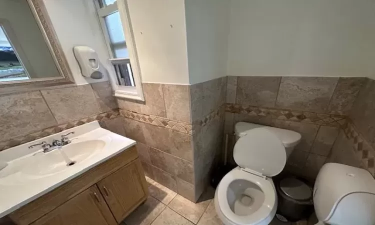 Bathroom with tile patterned floors, vanity, toilet, and tile walls