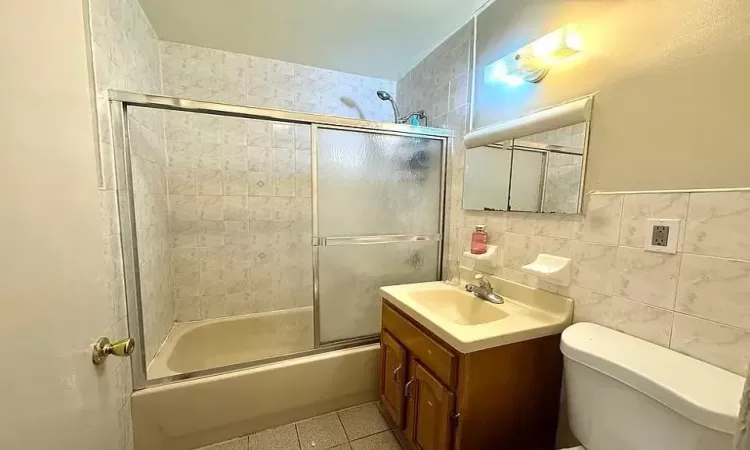 Full bathroom featuring vanity, shower / bath combination with glass door, tile patterned floors, toilet, and tile walls