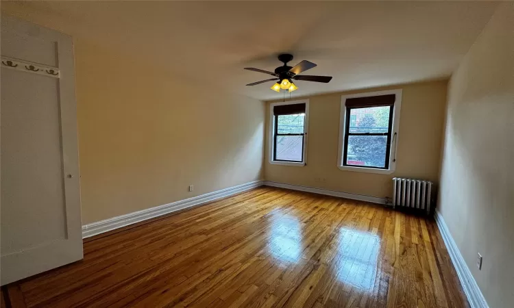 Unfurnished room featuring ceiling fan, radiator heating unit, and light wood-type flooring