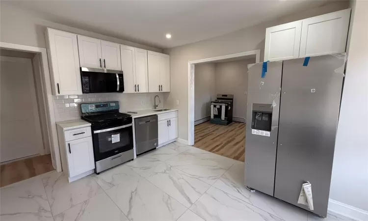 Kitchen featuring appliances with stainless steel finishes, backsplash, a baseboard heating unit, sink, and white cabinets