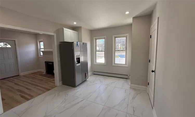 Kitchen featuring white cabinets, stainless steel fridge with ice dispenser, a baseboard radiator, and plenty of natural light