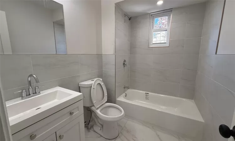 Full bathroom with toilet, vanity, tile walls, and tiled shower / bath