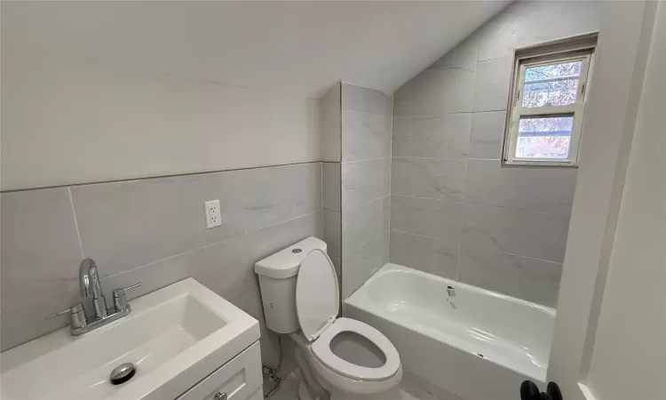 Bathroom with vanity, toilet, lofted ceiling, and tile walls