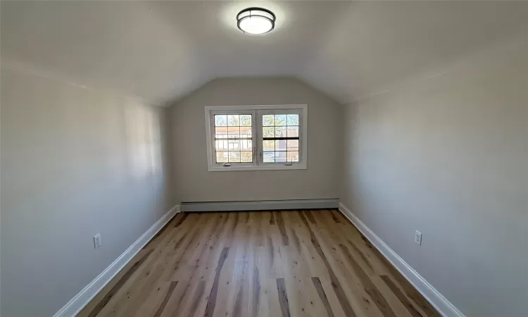 Additional living space with light hardwood / wood-style floors, vaulted ceiling, and a baseboard radiator