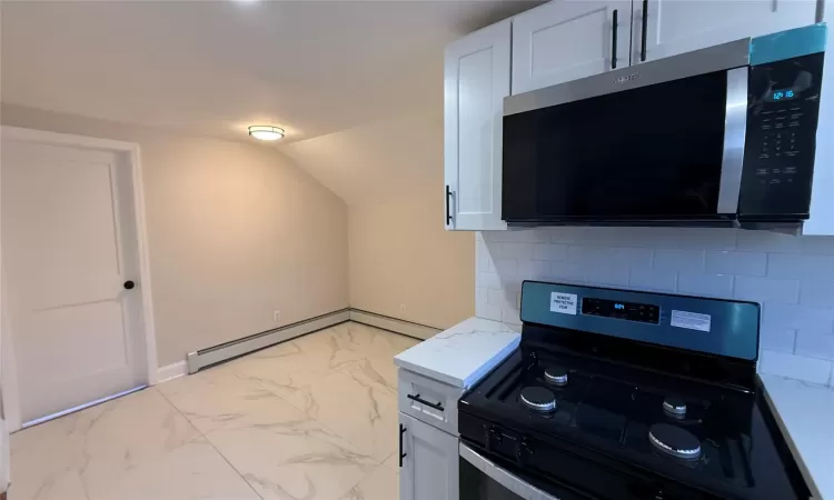 Kitchen with white cabinets, decorative backsplash, baseboard heating, and black range with gas cooktop