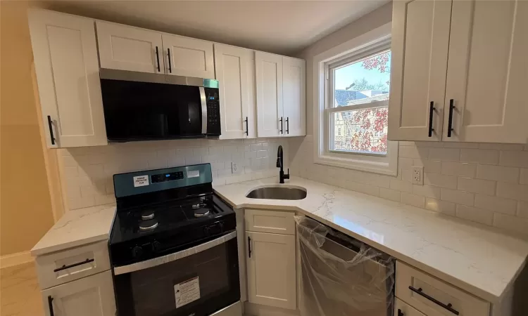 Kitchen featuring white cabinets, sink, decorative backsplash, light stone counters, and stainless steel appliances