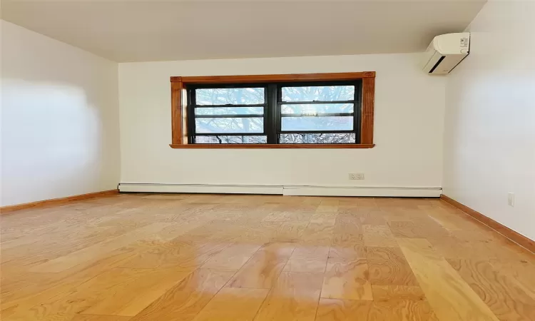 Empty room with a wall mounted AC, light hardwood / wood-style flooring, and a baseboard heating unit