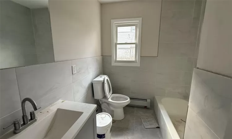 Bathroom featuring a bathtub, vanity, a baseboard heating unit, toilet, and tile walls