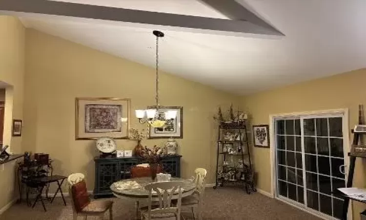 Dining space featuring carpet flooring, vaulted ceiling, and an inviting chandelier