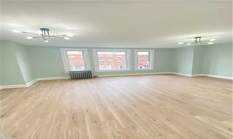 Unfurnished room with ceiling fan with notable chandelier, light hardwood / wood-style floors, and radiator heating unit