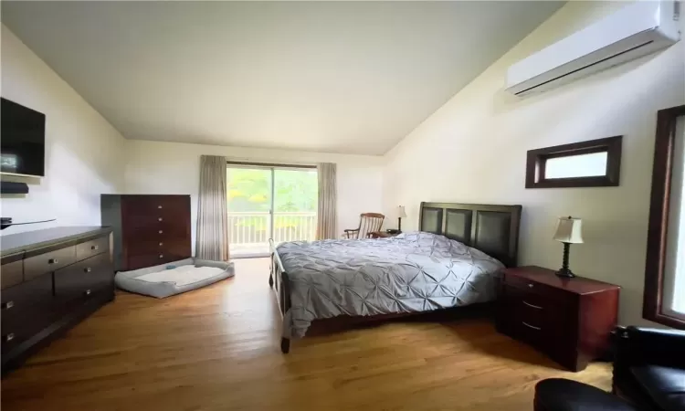 Bedroom featuring access to outside, light hardwood / wood-style flooring, a wall mounted air conditioner, and lofted ceiling