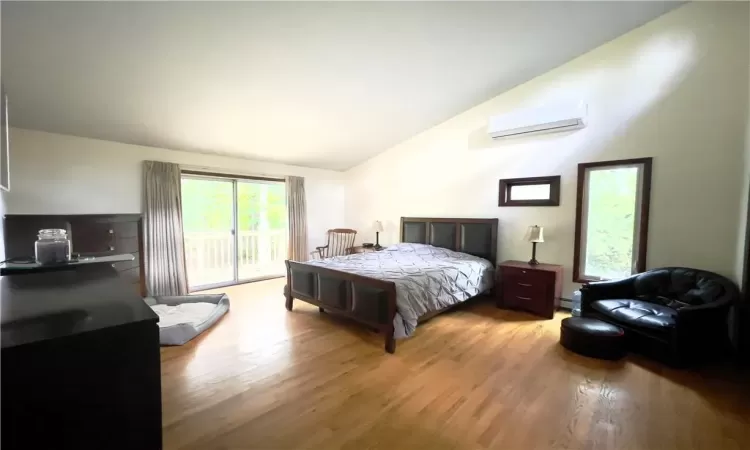 Bedroom featuring a wall mounted air conditioner, light wood-type flooring, access to exterior, and lofted ceiling