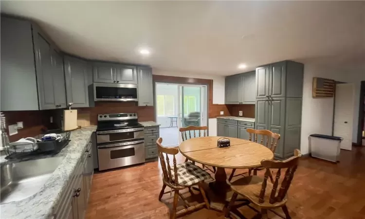 Kitchen with light hardwood / wood-style floors, sink, gray cabinetry, appliances with stainless steel finishes, and light stone countertops