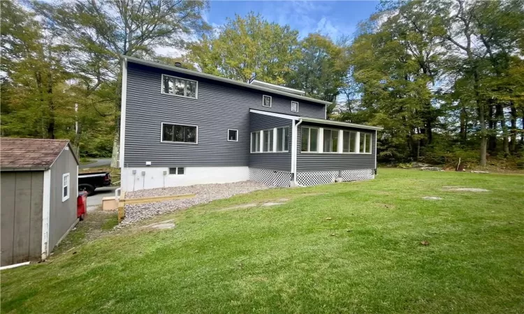 Rear view of property featuring a shed, a yard, and a sunroom