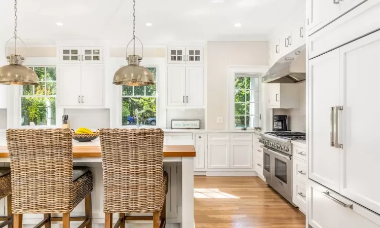 Kitchen featuring pendant lighting, high end appliances, white cabinetry, and tasteful backsplash