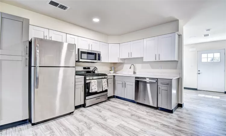 Kitchen featuring gray cabinetry, sink, light wood-type flooring, and appliances with stainless steel finishes