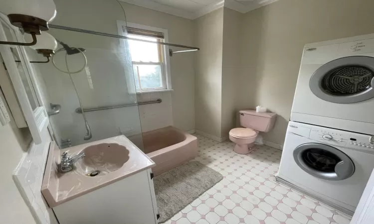 Full bathroom featuring stacked washing maching and dryer, vanity, tiled shower / bath combo, crown molding, and toilet