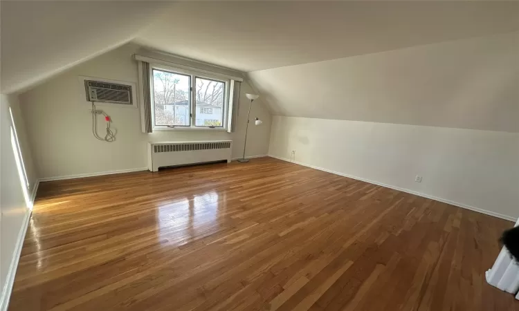 Bedroom featuring wood-type flooring, radiator heating unit, a wall mounted AC, and vaulted ceiling