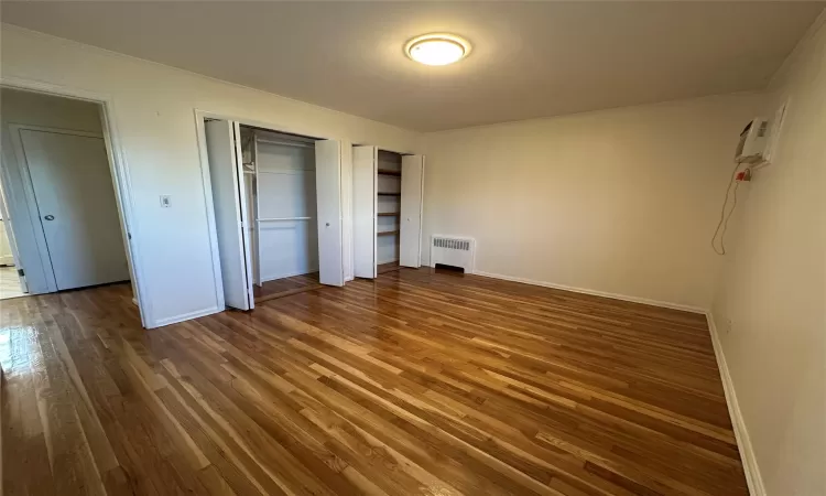 bedroom bedroom with a wall mounted AC, dark hardwood / wood-style flooring, radiator, and two closets