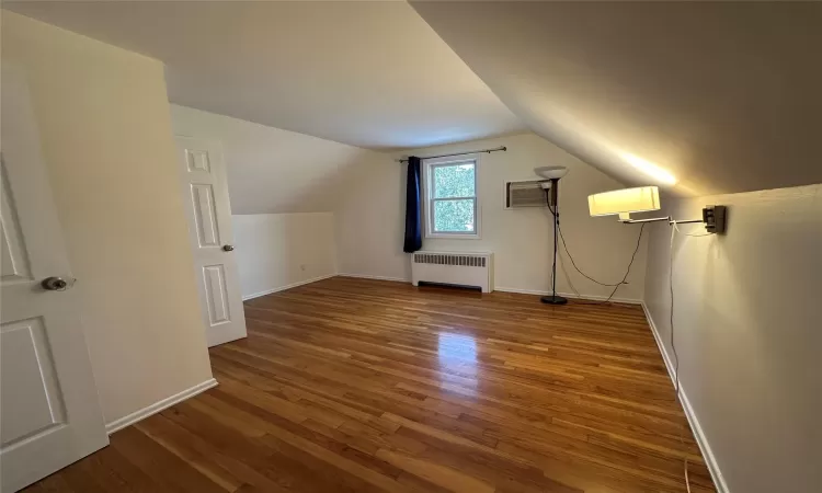 Bonus room with an AC wall unit, radiator heating unit, wood-type flooring, and vaulted ceiling