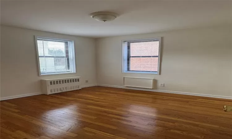 Spare room with a wealth of natural light, dark hardwood / wood-style flooring, and radiator