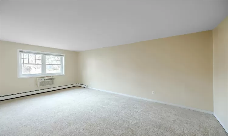 Carpeted spare room featuring a wall unit AC and a baseboard radiator