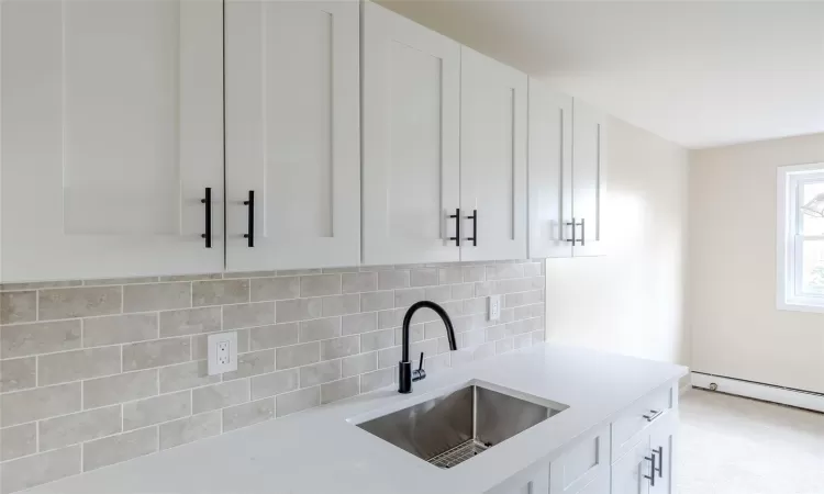 Kitchen with white cabinets, a baseboard radiator, tasteful backsplash, and sink