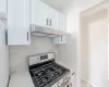 Kitchen with white cabinets, gas range, backsplash, and extractor fan