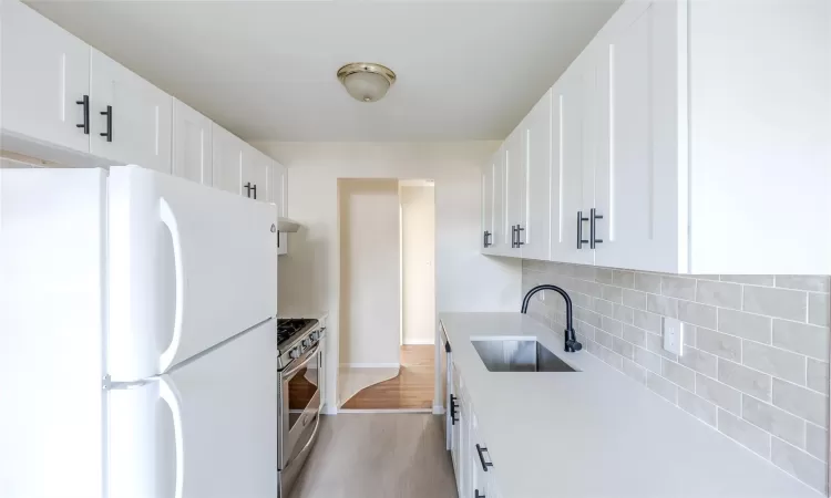 Kitchen featuring light wood-type flooring, sink, white refrigerator, white cabinets, and stainless steel gas stove