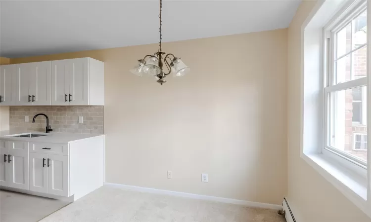 Kitchen with sink, tasteful backsplash, a baseboard heating unit, pendant lighting, and white cabinets