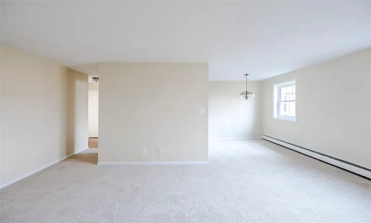 Carpeted empty room with an inviting chandelier and a baseboard radiator