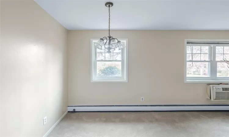 Unfurnished room with carpet, a notable chandelier, a wall unit AC, and a baseboard heating unit