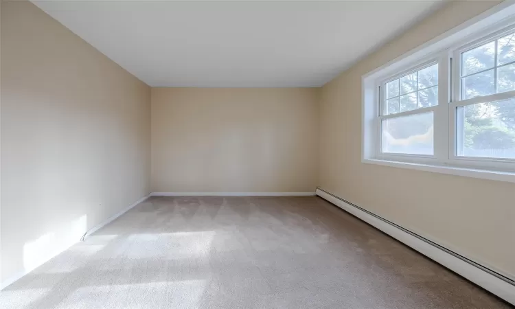 Unfurnished room with light colored carpet and a baseboard radiator