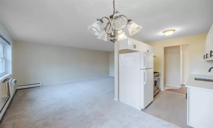 Kitchen with white cabinetry, sink, baseboard heating, white refrigerator, and decorative light fixtures