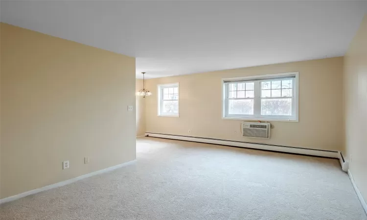 Empty room with a wall mounted air conditioner, a notable chandelier, baseboard heating, and light carpet