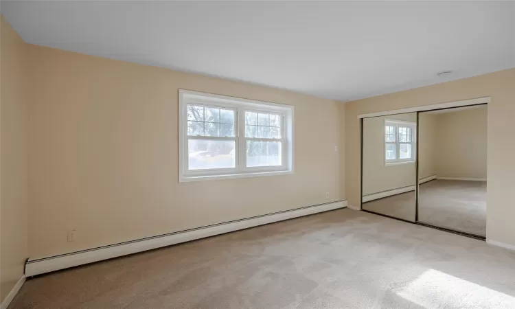 Unfurnished bedroom featuring a closet, light colored carpet, and a baseboard radiator