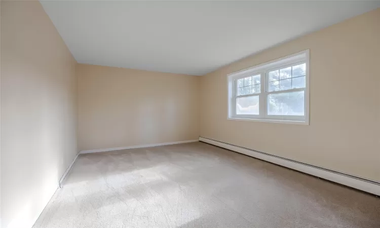 Unfurnished room featuring light carpet and a baseboard heating unit