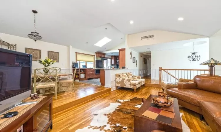 Living room featuring lofted ceiling with skylight, an inviting chandelier, and light wood-type flooring