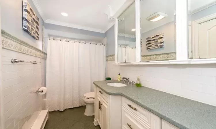 Bathroom with vanity, toilet, tile walls, and crown molding