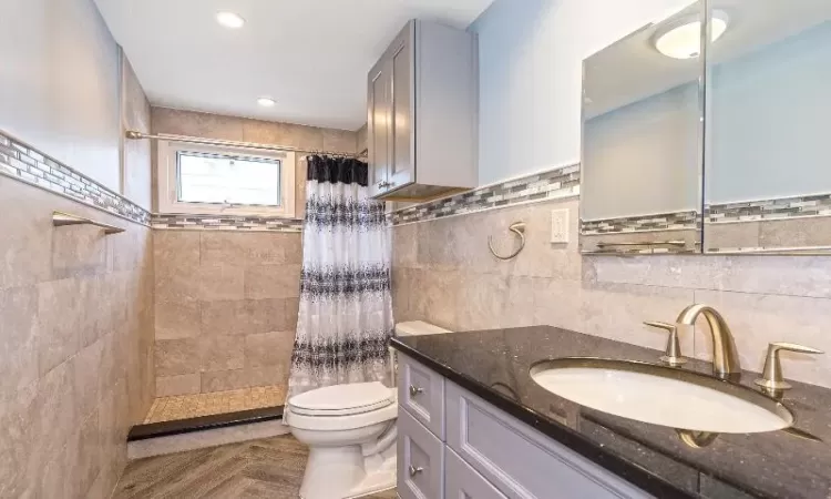 Bathroom featuring a shower with shower curtain, vanity, toilet, and tile walls