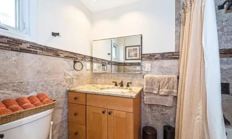 Bathroom featuring vanity, toilet, and tile walls