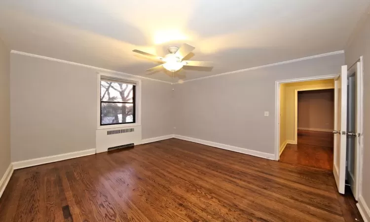 Empty room with ceiling fan, dark hardwood / wood-style flooring, radiator heating unit, and crown molding